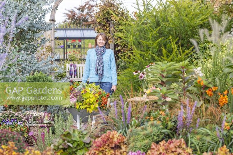 Woman pushing wheelbarrow full of plants through garden