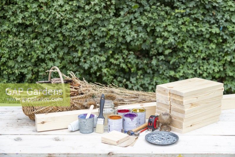 20 wooden planks (9.5cm x 30cm x 2cm), wooden post (7cm x 7cm x 210cm), wooden square (9.5cm x 9.5cm x 2cm), paint, paintbrush, hammer, nails, sandpaper, cloth, pencil, tape measure, bamboo, pine cones, bark, dried leaves, dried grass, moss, teasels laid out on a table