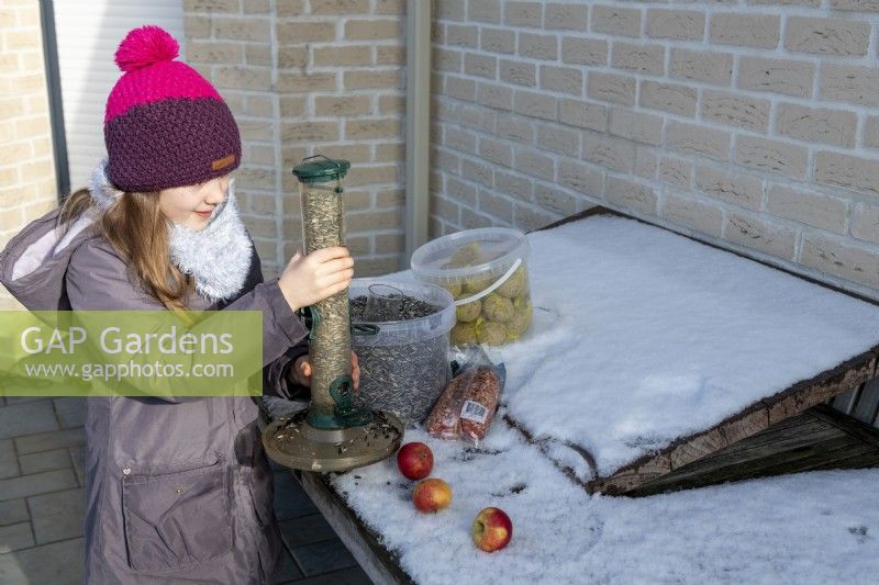 Girl holding bird feeder filled with sunflower seeds on snowy day in winter