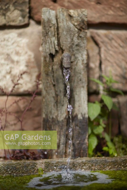 Water feature. Very old rusty iron water spout on old stone wall. Summer. Garden Shows. 