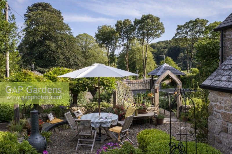 Gravel patio area with outdoor garden table and chairs, parasol and chiminea