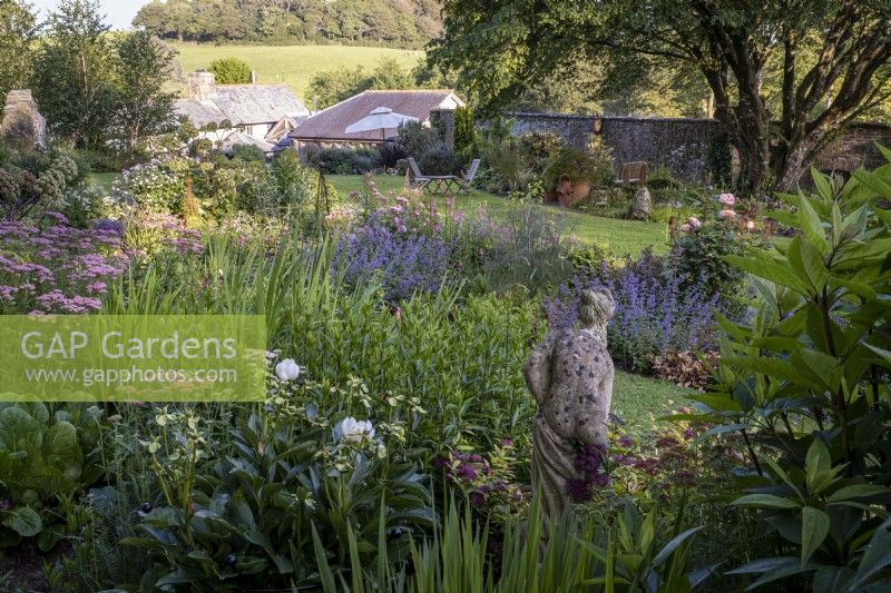 Classical statue of a woman, hidden amongst deep perennial summer borders, in a country garden in Cornwall