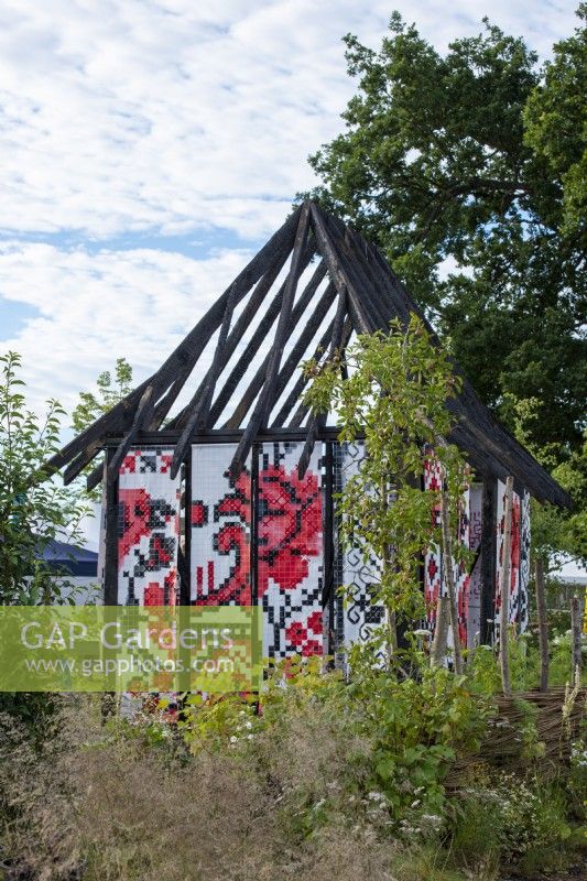 Representation of a Ukranian burnt cottage draped with rushnyk, an embroidered cloth.  What Does Not Burn - RHS Hampton Court Palance Garden Festival 2022