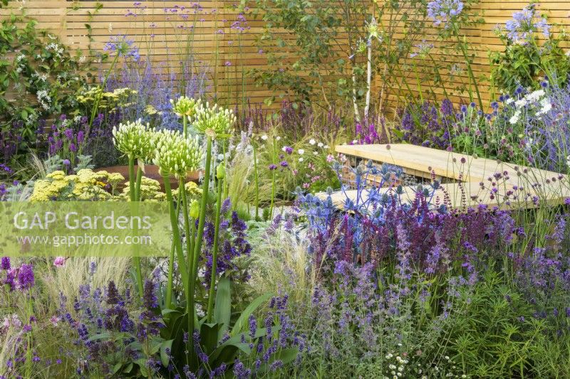 Bug hotel gabion bench with wooden  top in low maintenance gravel garden with drought tolerant plants to attract pollinators, such as Salvia, Achillea, Agapanthus, Stachys byzantina, Nepeta and Stipa tenuissima- Turfed Out, RHS Hampton Court Palace Garden Festival 2022