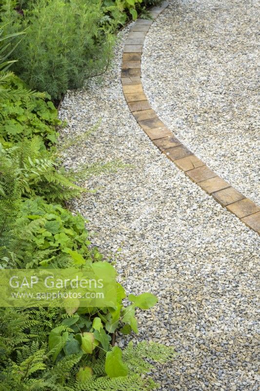 Winding gravel path with wooden pattern through perennial mixed planting in A Journey, in Collaboration with Sue Ryder garden at RHS Hampton Court Palace Garden Festival 2022