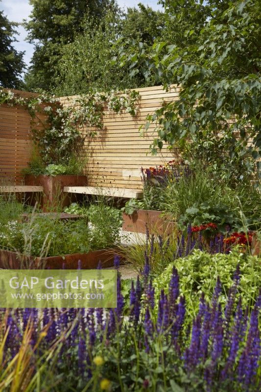 'Lunch Break Garden'. Seating area with contemporary wooden  fencing and Corten steel planters. RHS Hampton Court Palace Garden Festival, London, July 2022 - Best in Show Get Started Gardens - Designer: Inspired Earth Design