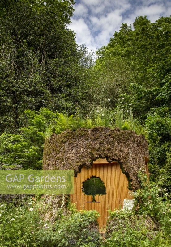 A woodland wildlife friendly garden with an oak tree trunk shelter with a living planted roof on the Connected by EXANTE Garden - RHS Chelsea Flower Show 2022 - Designed by Designer Taina Suonio - Built by Nicholsons 