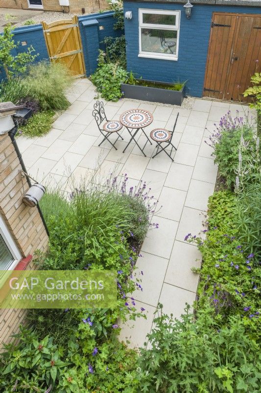 Aerial view of a modern patio garden in summer with plants chosen to encourage insects. Erysimum, geraniums, lavender, echinops, veronicastrum. Mosaic folding table and chairs, bee barrel hanging on wall. June.