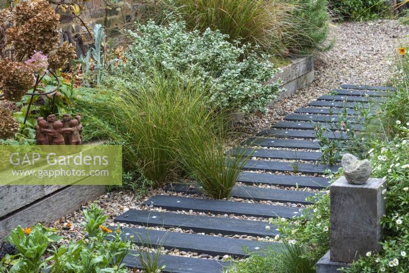 A path is made from wood off-cuts left over from laying the wooden decks, fixed at equal intervals beneath the gravel. Self-seeded grasses, marigolds and gaura have established.