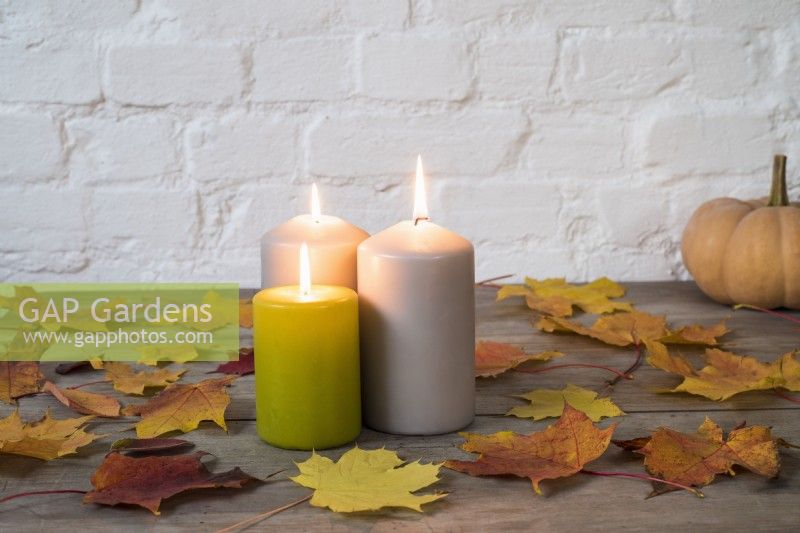 Trio of lighted pillar candles with autumn leaves and 'Autumn Crown' pumpkin on wooden background