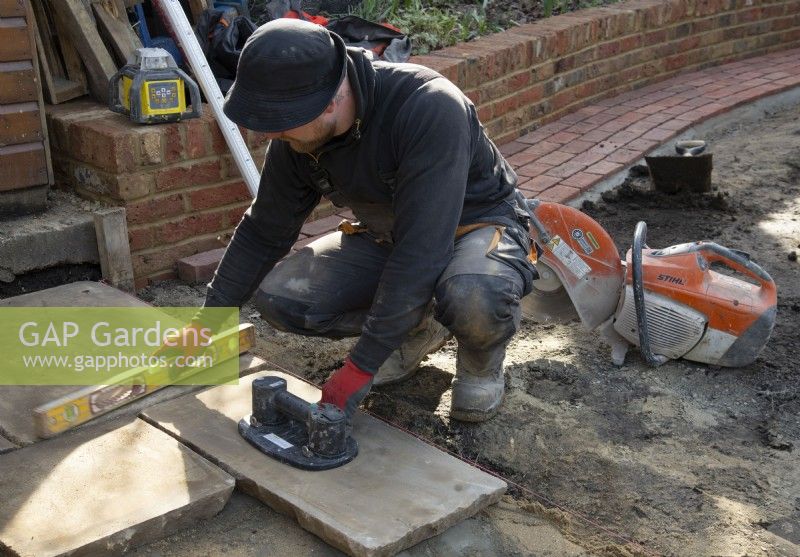 A worker laying slabs of York Stone for a terrace during the makeover of a small London garden.