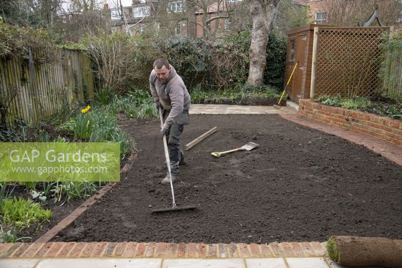 A worker raking the ground in preparation for laying new turf during the makeover of a London garden.