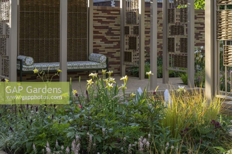 Herbaceous beds planted with  lupins,  white alliums, geums, astrantias, pimpinella, verbascums and ornamental grasses. in front of pavillion made of willow screens with seating - Stitchers Sanctuary Garden. Design: Frederic Whyte