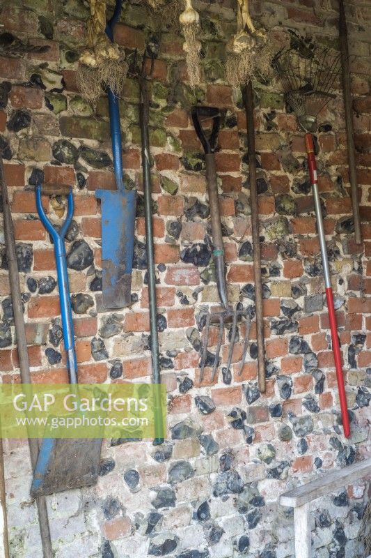Gardening tools hanging on a brick wall in potting shed