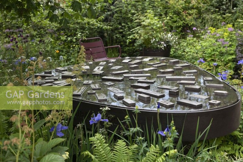 View of the interactive wheelchair friendly water feature with casting mould details based on the Sheffield cutlery industry. Surrounding plants include Iris sibirica Silver Edge -  Siberian iris Silver Edge and Rodgersia podophylla - Rodgers' bronze-leaf.

Horatio's Garden at RHS Chelsea Flower Show 2023.

Design: Harris Bugg Studio