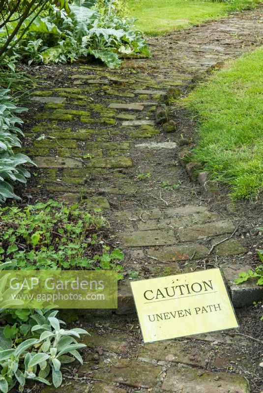 Warning sign on uneven brick path - Open Gardens Day, East Bergholt, Suffolk