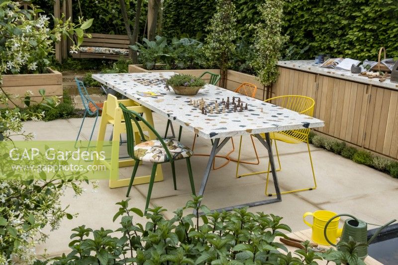 A community table that incorporates two chess boards and is place for people to come together to eat or play games. Plants in the foreground,Trachelospermum jasminoides and Mentha Ã— piperita. The London Square Community Garden, Gold winner - Designer: James Smith