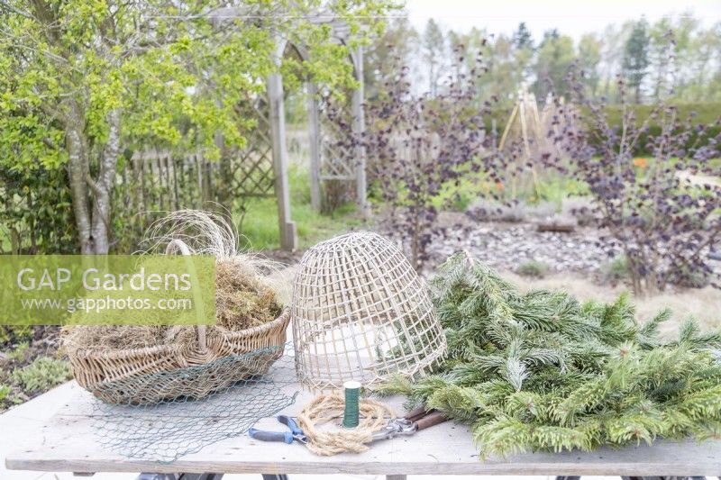 Dried grass, moss, pine branches, bamboo cloche, chicken wire, wire, secateurs, wire cutters and rope laid out on table