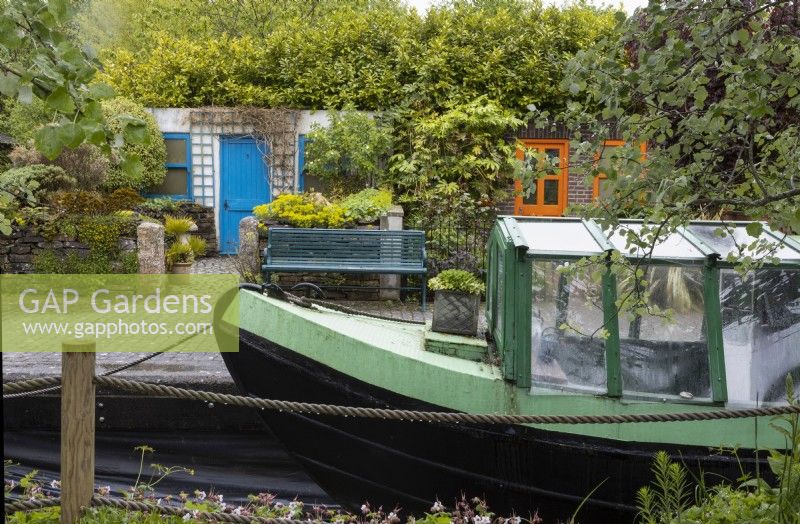 Canal Street garden with a real barge and canal lock beside a terraced street with four small front gardens of differing designs including a cottage, formal parterre and classic town garden. Trago Mills show gardens, Devon, UK. May. Spring