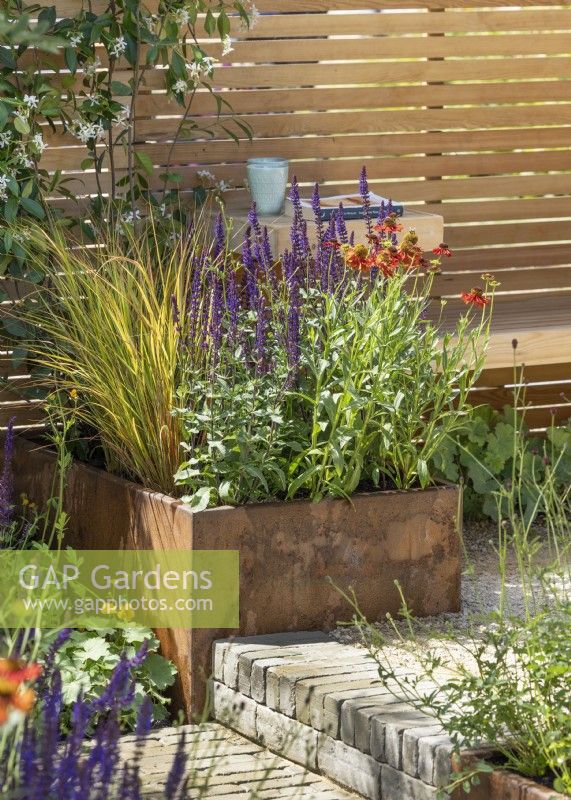 Terrace garden with square plant container next to step, summer July