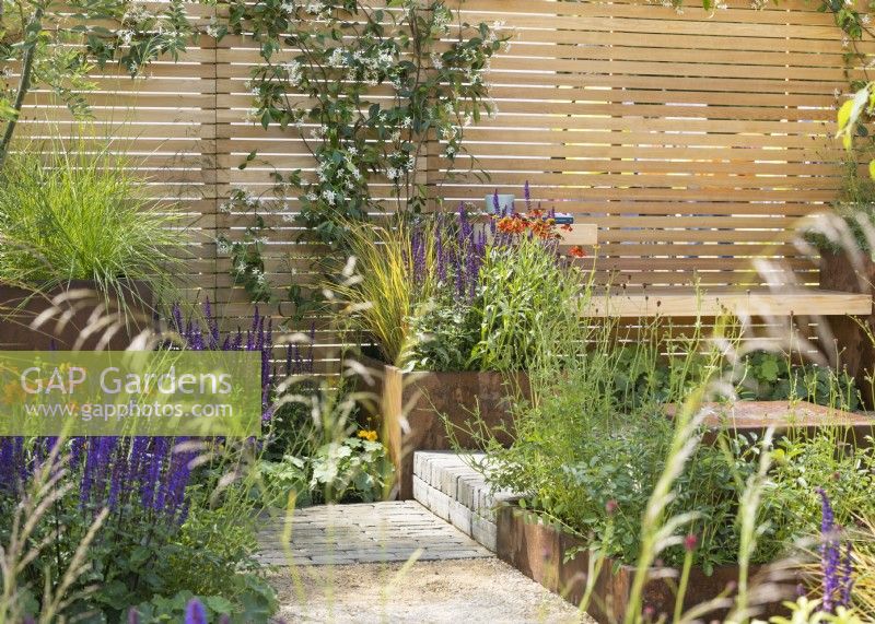 Terrace garden enclosed by fence, with square containers of perennials alongside path, summer July