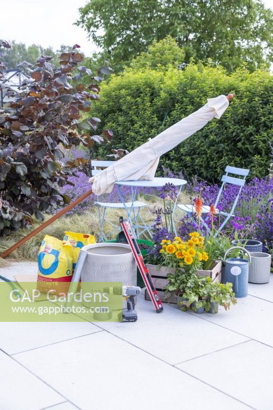 Parasol, Postcrete, scaffolding pole segment, sprit level, drill, duct tape, hosepipe, watering can and mixed plants laid out on ground