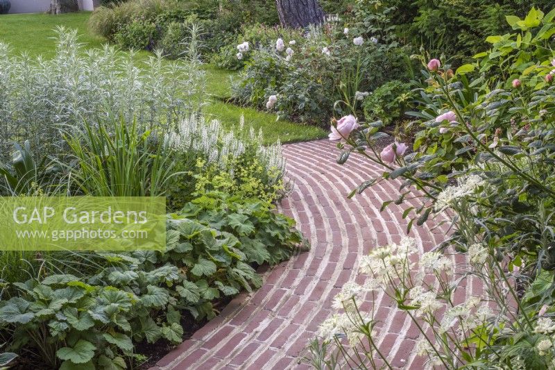 Terracotta brick curved running bond path; border plants include Rosa 'Queen of Sweden' and Salvia sylvestris 'Schneehugel'; Astrantia major 'Large White'