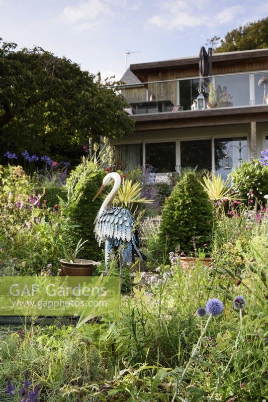 July garden full of lush planting around a metal heron decoy sculpture