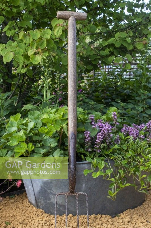 Border fork leaning against recycled metal container with planting - RHS Malvern Spring Festival 2023 - Bee Positive, Bee Kind, Bee Aware - Designers Rick Ford, Katie Gentle