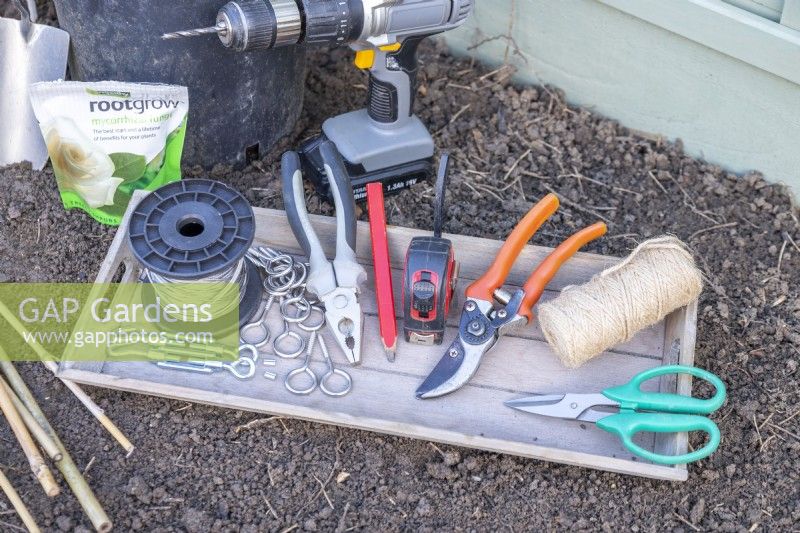 Wire, eyelet screws, ferrules, tensioners, pliers, pencil, tape measure, secateurs, string and scissors on wooden tray