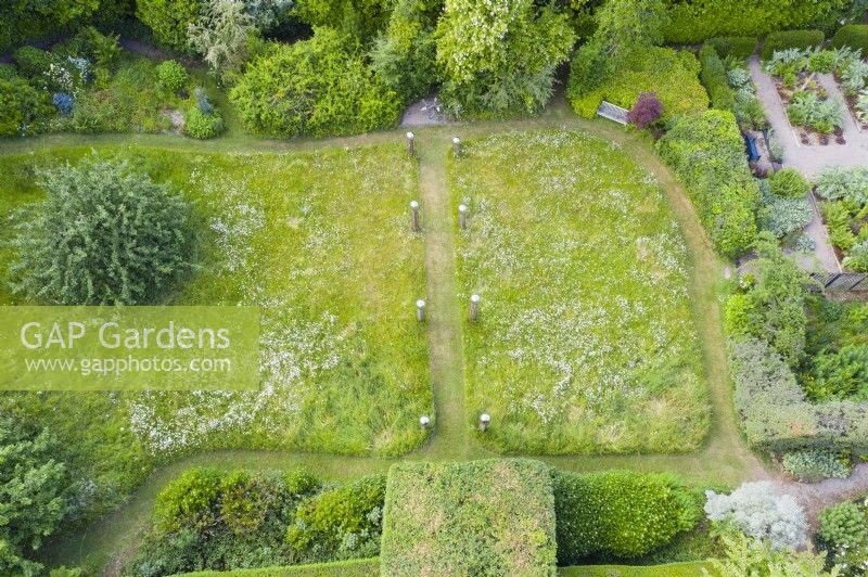 View over meadow with formal avenue of cut grass lined with wooden posts topped with stainless steel globes. June. Summer. Image taken with drone. 