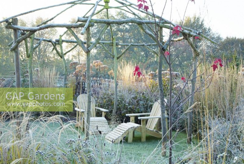 Frosted, rustic coppiced ash gazebo and wooden sun loungers surrounded by perennial grasses and seedheads.