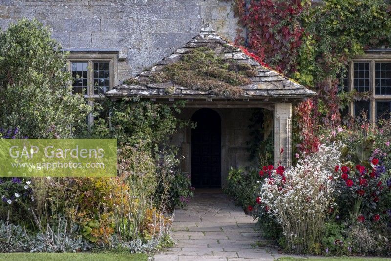 Informal overflowing autumnal borders with grasses and perennials, including Dahlia 'Dovegrove', Fennel, and Salvia. Old tiled porch at Gravetye Manor Gardens