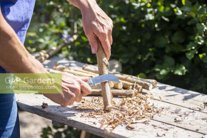 Woman carving bark away from a stick to create a flat surface on one side