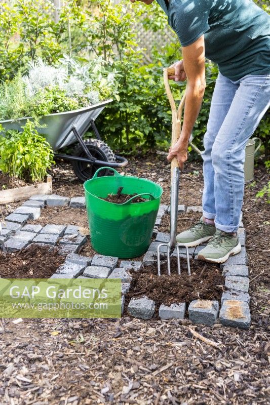 Woman mixing in compost with the soil in the open squares