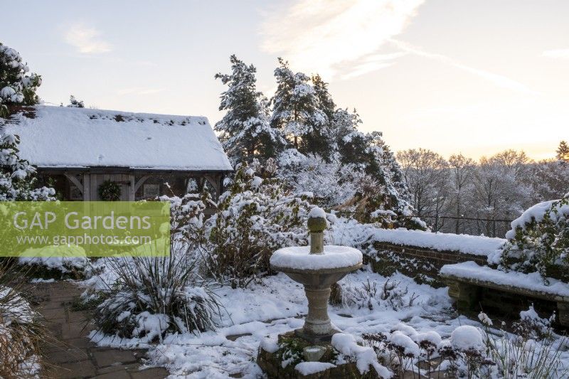 The garden at Gravetye Manor, Sussex, in winter. A view across the small garden to the oak framed summerhouse.  Sundial in snow