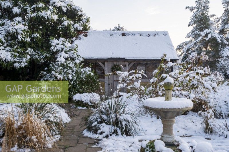 The garden at Gravetye Manor, Sussex, in winter. A view across the small garden to the oak framed summerhouse.  Sundial in snow