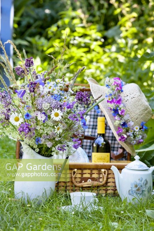Set for picnic with wildflower bouquet in a jug and a hat with a wreath.