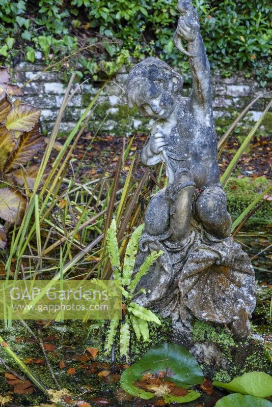 Figure of boy on a dolphin in a pond at Compton Acres, Dorset in November