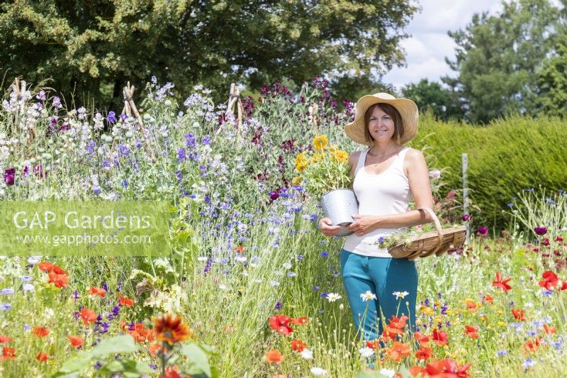 Woman holding a bucket and a trug of picked seed pods