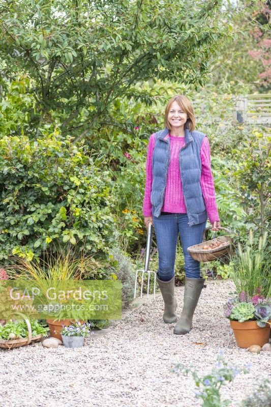 Woman walking along gravel path carrying a digging fork and a trug full of tulip bulbs