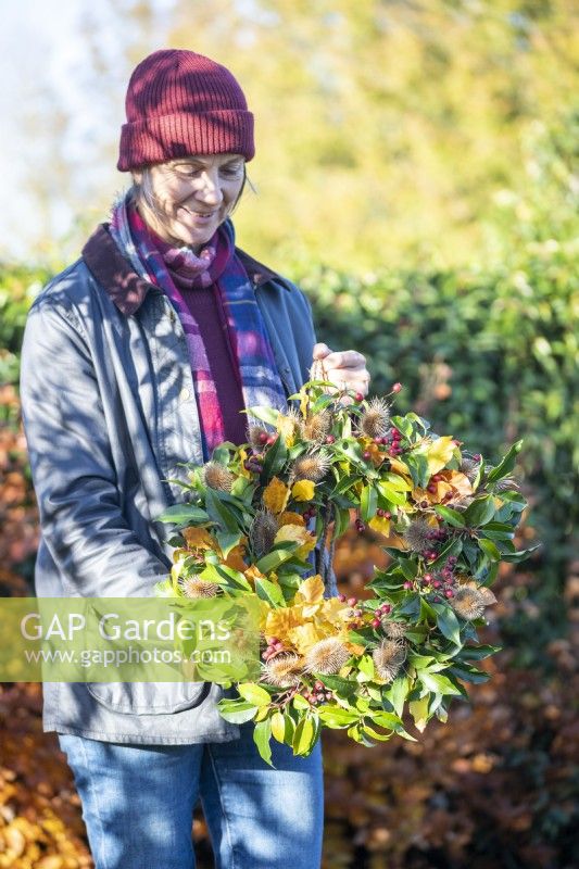 Woman holding up wreath made up of Beech sprigs, Portuguese laurel sprigs, Teasel heads and Hawthorn twigs