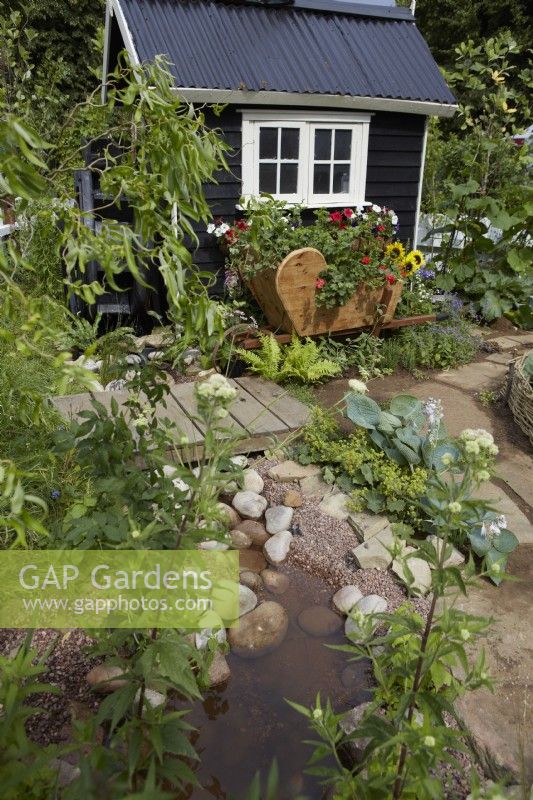 Southend City Council: The Miller's Garden. Designer: Tony Wagstaff. Shallow water rill and black painted shed amongst vegetables in a 'working' garden. Summer.