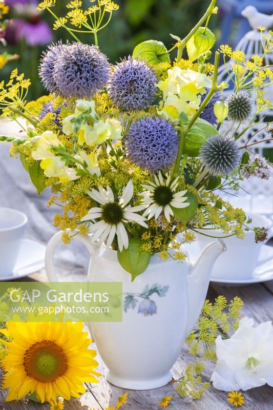 Yellow - blue - white themed bouquet consisting of Echinops, Snapdragon, Fennel, Echinacea, Achillea and Physalis in a teapot.