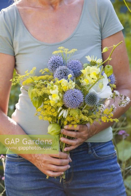 Woman with bouquet of white - blue - yellow flowers including Echinops, Snapdragon, Fennel, Echinacea, Achillea and Physalis.