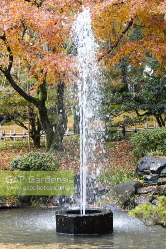 Fountain in small pool, said to be the oldest fountain in Japan, dating from the C19th and fed by the Kasumigaike pond. Trees in autumn colour behind. 