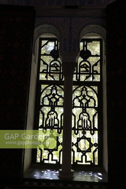 Ornate, Moorish style windows in the Real Alcazar Palace give a hint of green to the gardens outside. Seville. Spain. September. 