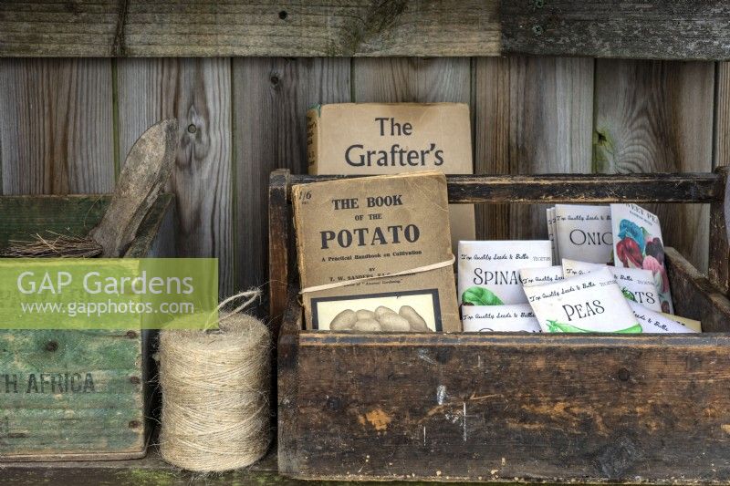 Wooden boxes with vintage gardening books, seeds bags and gardening twine placed on a shelf