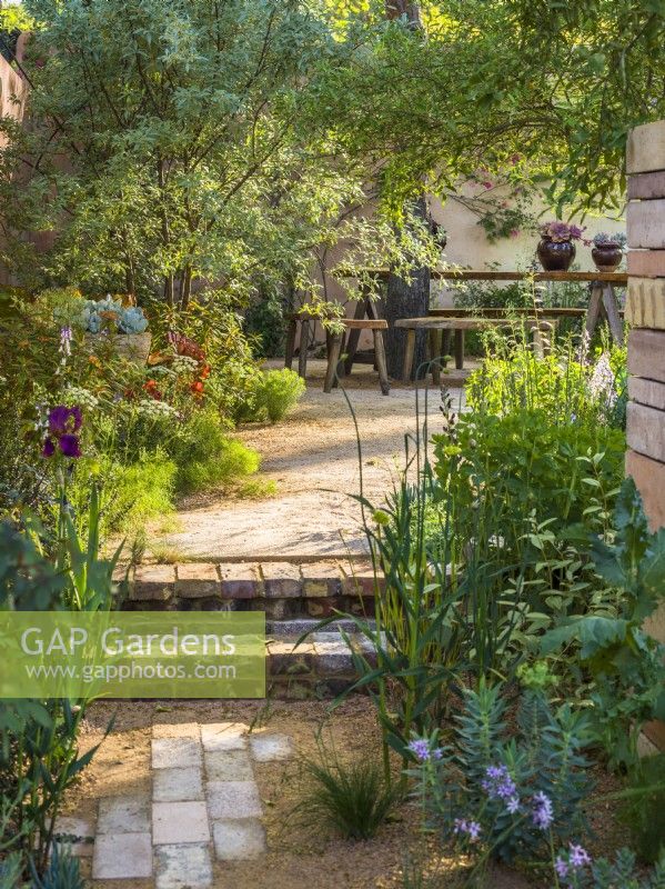 Path and steps made of bricks and gravel leading to dining area. The Nurture Landscapes Garden, Designer: Sarah Price, Gold medal winner Chelsea Flower Show 2023
