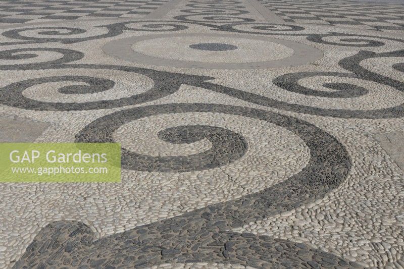 A large, flat open area is cobbled in black and white pebbles and laid out in a symmetrical and geometric pattern. Plaza de Espana, Parque de Maria Luisa, Seville, Spain. September